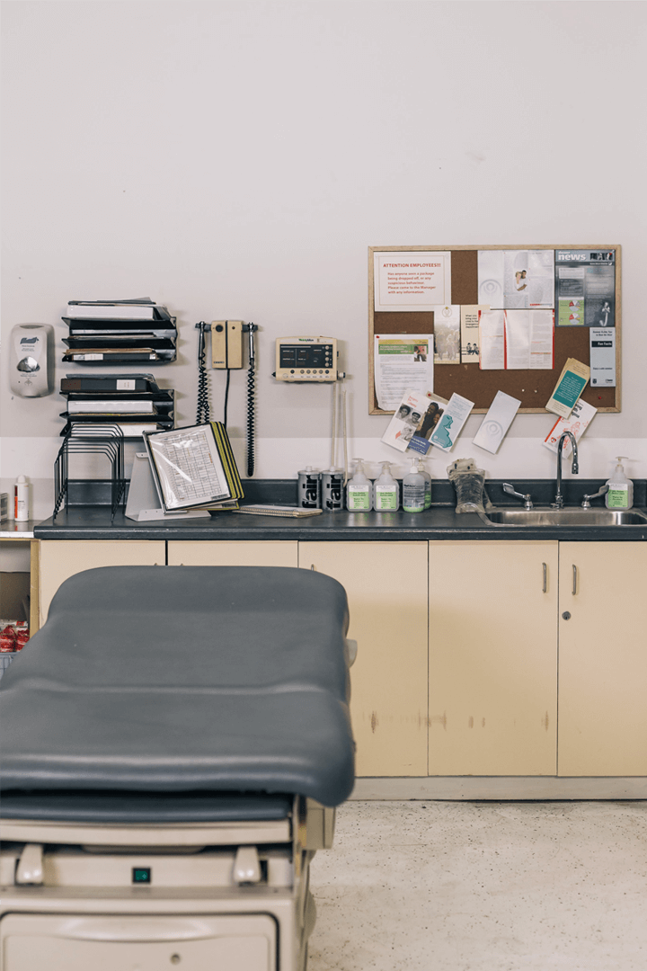 A hospital checking room with various medical equipment and consumables neatly arranged, including diagnostic tools, gloves, syringes, and medical supplies on shelves and countertops.
