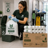 A woman in a green Bionest uniform kneels beside a compostable garbage bag dispenser, handling a large white bag printed with the Bionest logo. In front of her are multiple rolls of compostable bags and a brown cardboard box labeled 82L, all branded Bionest, in a clean indoor facility setting.