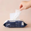 Hand reaching for a Snugz water wipe from its packaging on a beige background